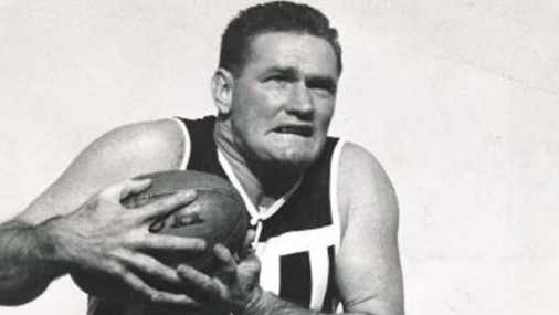 A black and white photo of a man clutching a football to his chest with one leg in the air