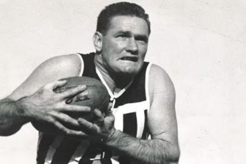 A black and white photo of a man clutching a football to his chest with one leg in the air