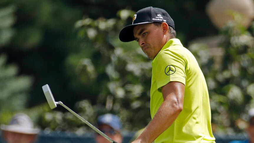 Rickie Fowler watches a put wearing a bright yellow golf shirt.