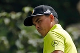 Rickie Fowler watches a put wearing a bright yellow golf shirt.