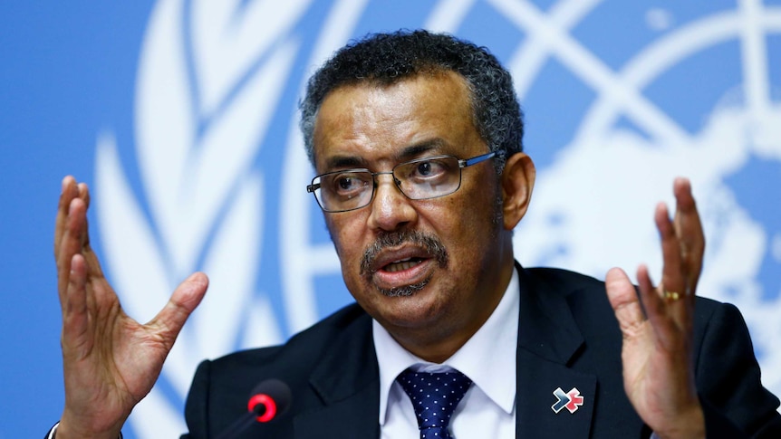 Tedros Adhanom Ghebreyesus sits at a microphone and gestures with his hands.