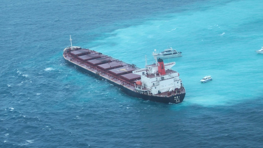 Ariel shot of a large coal carrier grounded on a part of the Great Barrier Reef surrounded by three other boats.