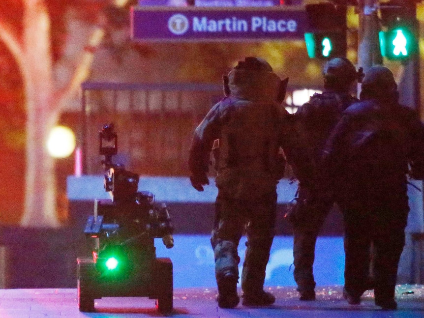 Police officers wearing armoured suit walk with robot in Martin Place