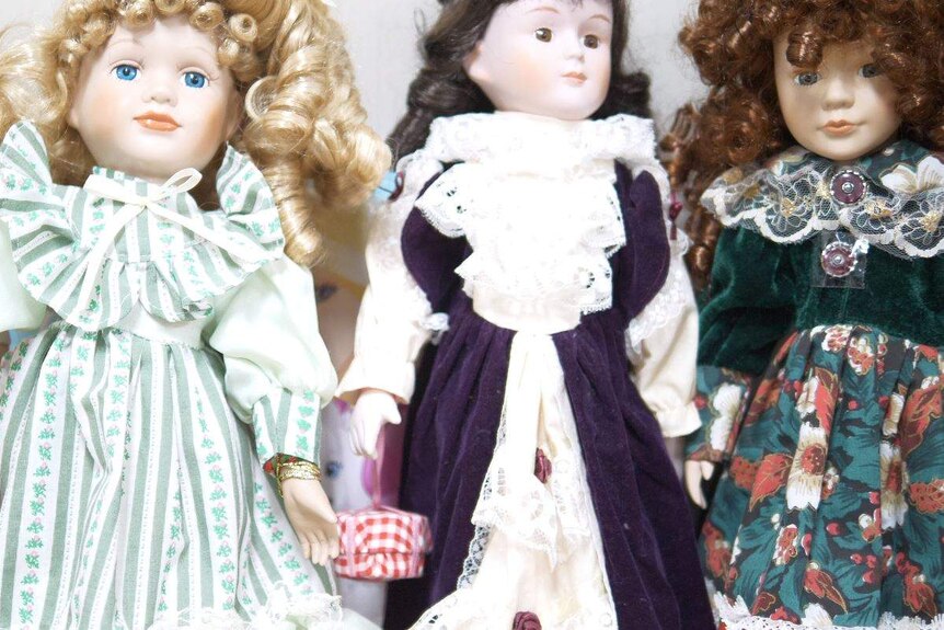 Four porcelain dolls are seen wearing various frilly dresses. They all have curly hair and blank stares.