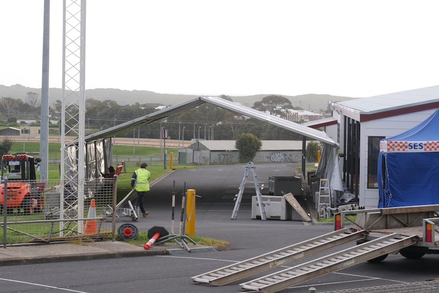 a worker in hi-vis sets up a large marquee next to a football oval