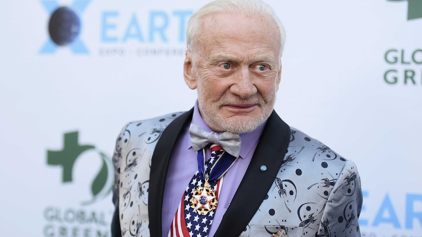 Buzz Aldrin wearing a stars and stripes tie and grey space themed jacket.