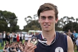 A young football player holds a medal around his neck.