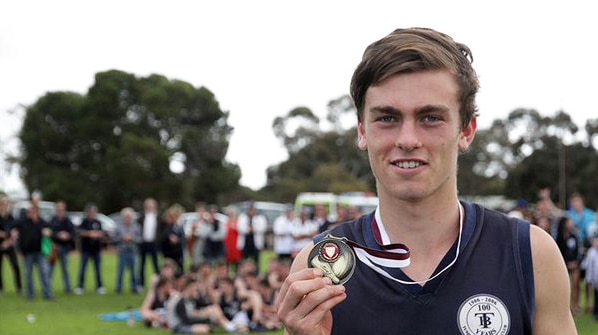 A young football player holds a medal around his neck.