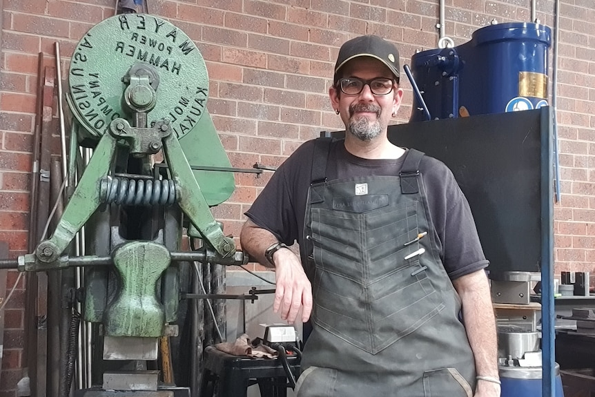 man stading in a workshop shed leaning on some equipment 