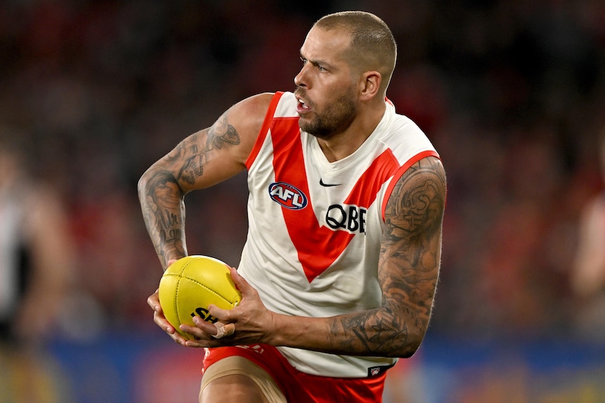 A Sydney Swans AFL player holds the ball in both hands during a match.