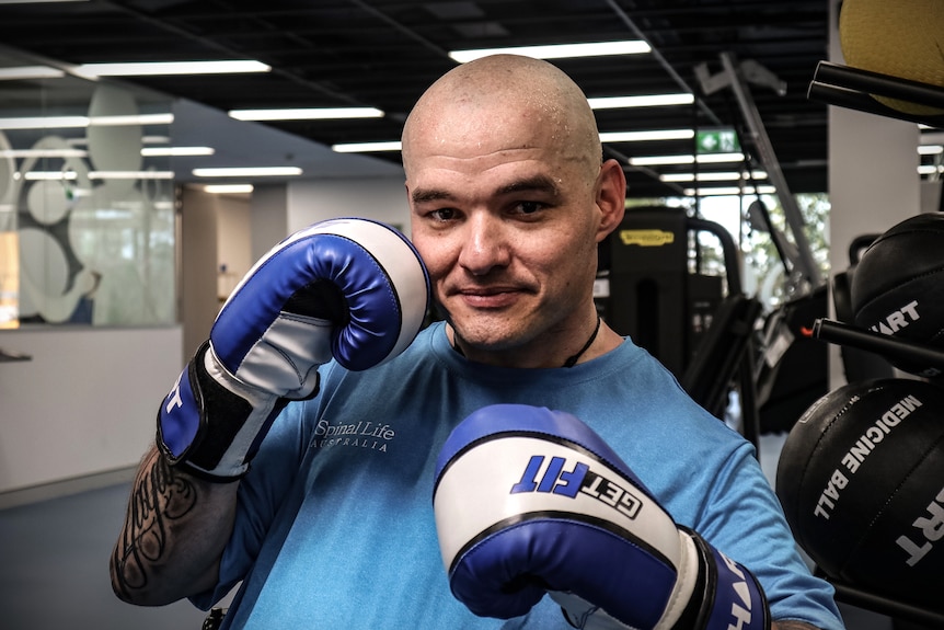 A bald man with boxing gloves looks at the camera.
