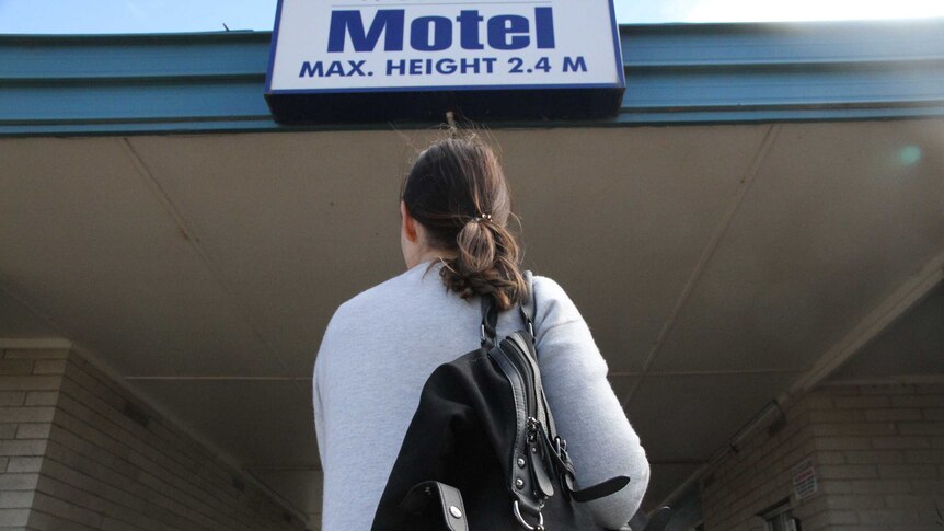 woman with duffle bag under a motel sign