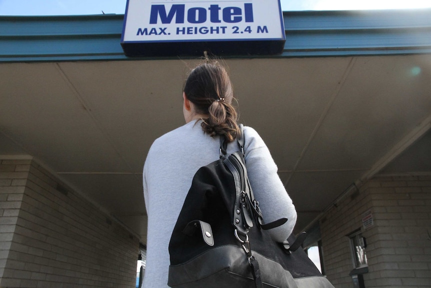 woman with duffle bag under a motel sign