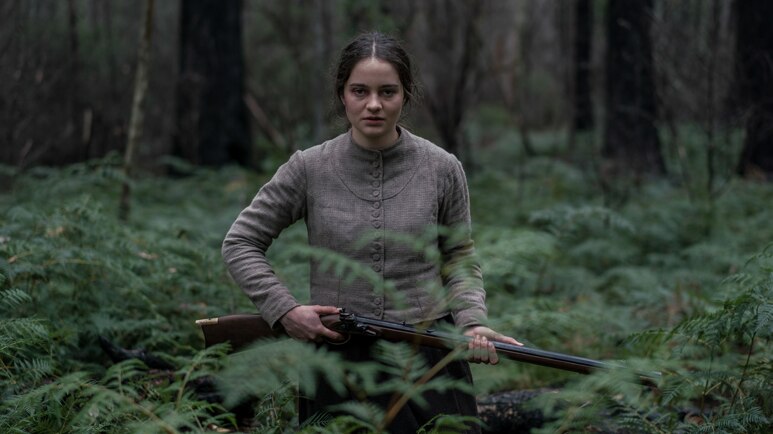 An actor carrying a rifle in the forest.