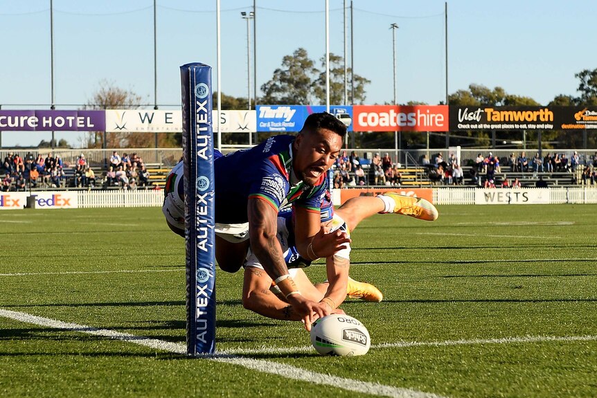 A Warriors NRL player dives in the air as he grounds the ball to score a try in the right-hand against Newcastle.