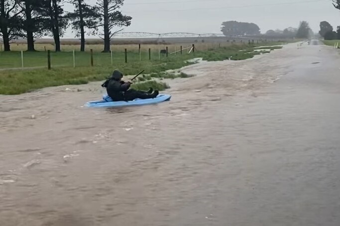 A man paddles a canoe in floodwater.