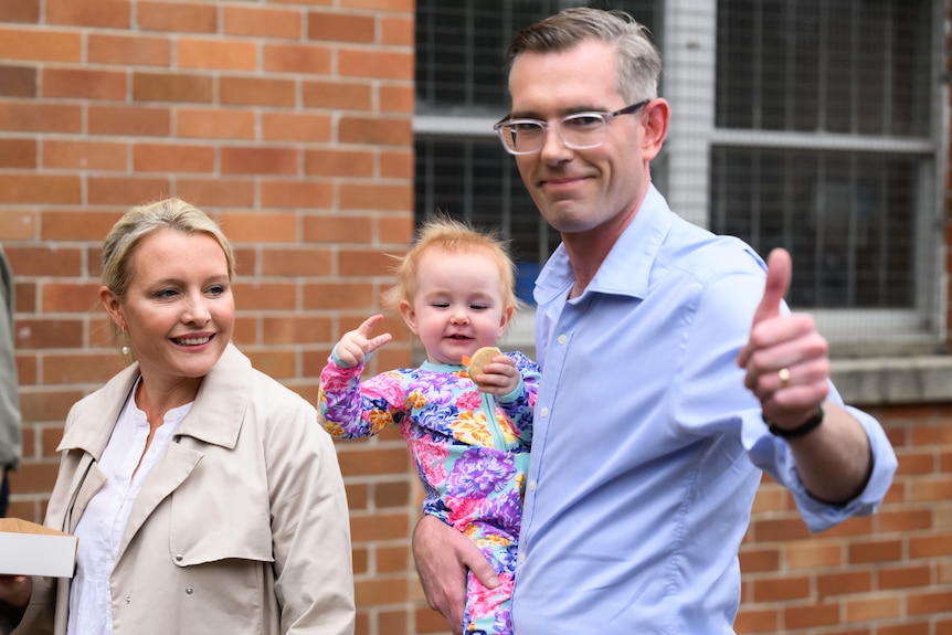 A man holding thumbs up with baby and a wife 