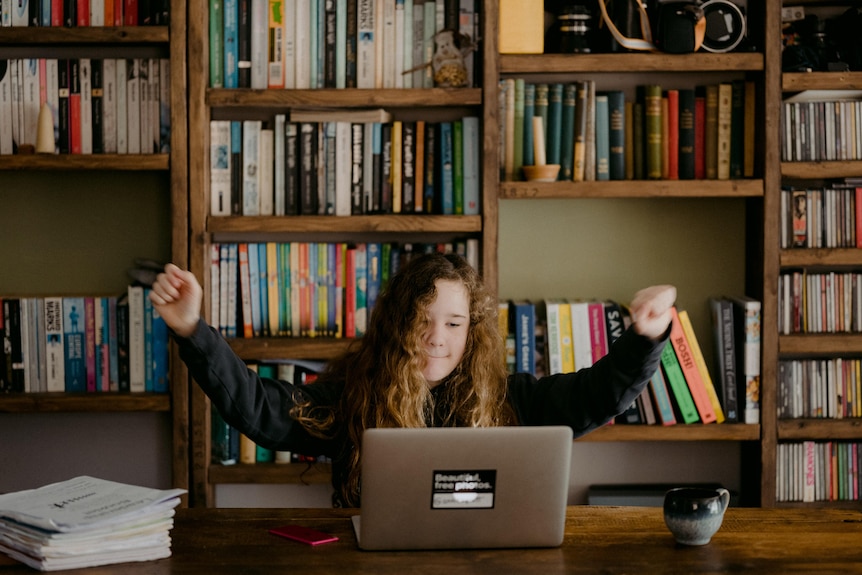 Teenage girl in front of laptop with arms up