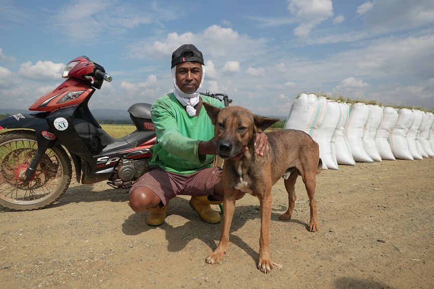 A man crouches in front of a motorbike with his dog.