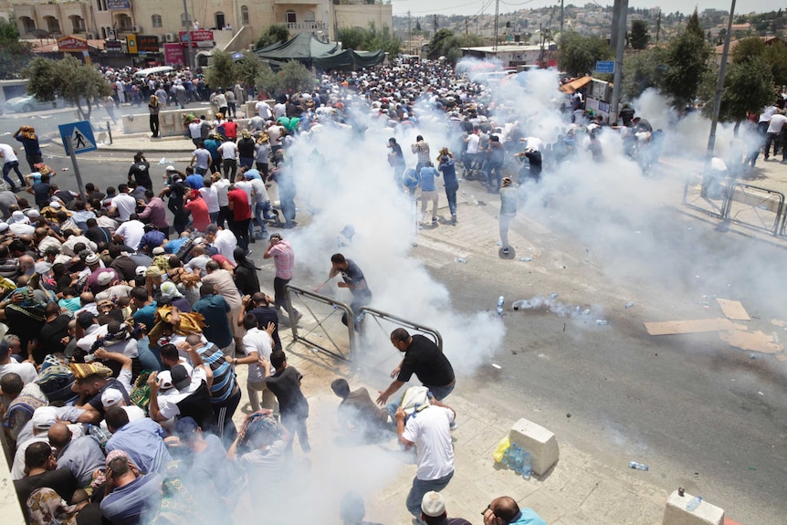 A crowd of thousands of people runs away from clouds of tear gas.