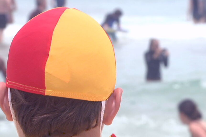 Back of a lifeguard's head looking at swimmers on Bondi Beach.