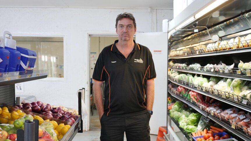A man stands between two supermarket shelves of fruit and vegetables 