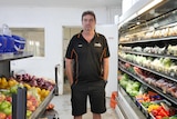 A man stands between two supermarket shelves of fruit and vegetables 