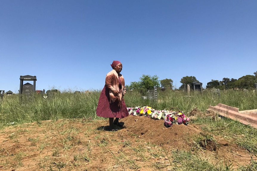 An old woman cries beside a fresh gravesite.