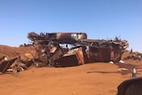 The mangled wreckage of an iron ore train sits on red dirt under a blue sky.