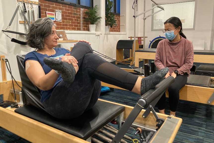 A woman in active wear stretching with another woman sitting by her.