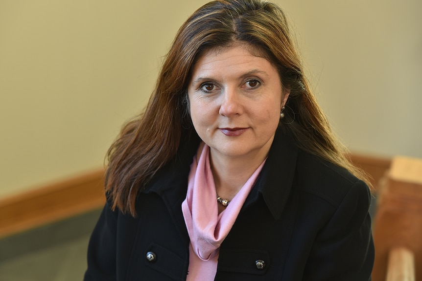 Betsey Stevenson, who has long brown hair, poses for a photo wearing a black blazer and pink top