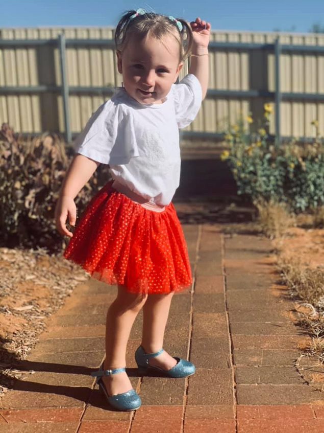 A little girl on a garden path in a red frilly skirt.