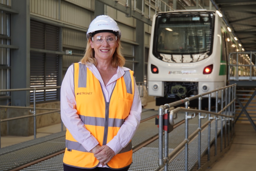 Rita Saffioti wearing an orange hi-vis, safety helmet and glasses stands in front of a new white train.