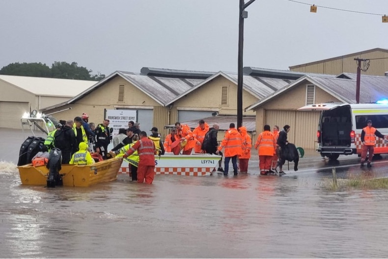 Emergency services in high viz launching boats into floodwater on a road.