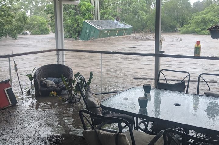 Flooding in the yard and verandah surrounding chairs, with a shipping container on its side in the distance.