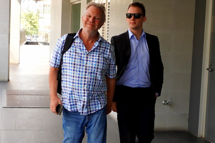 An older man on the right wearing a chequered shirt and jeans leaves court with Alister Swift dressed in a suit and sunnies.