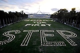 Candles form the words 'Sorry, The First Step' outside Parliament House