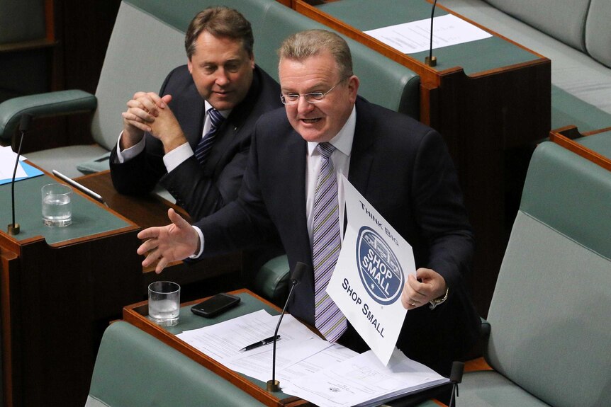 View from above of Bruce Billson, holding a sign, standing and speaking in the House of Representatives.