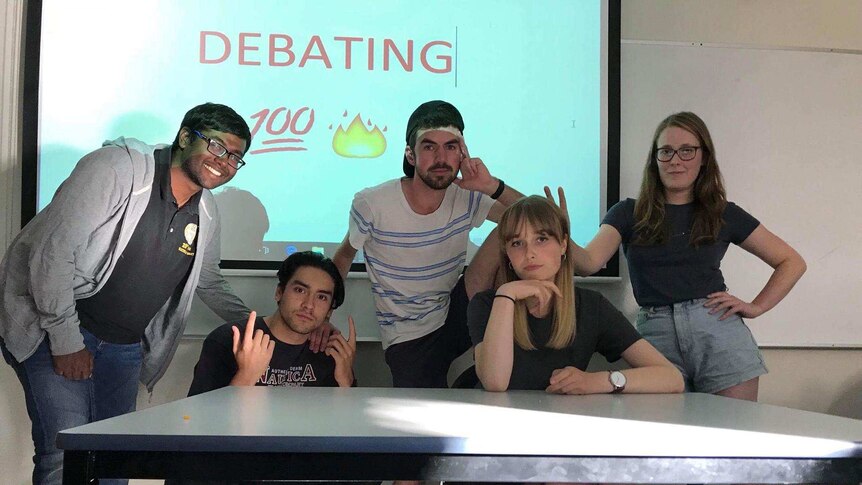 Picture of a group of five people with a debating sign behind them