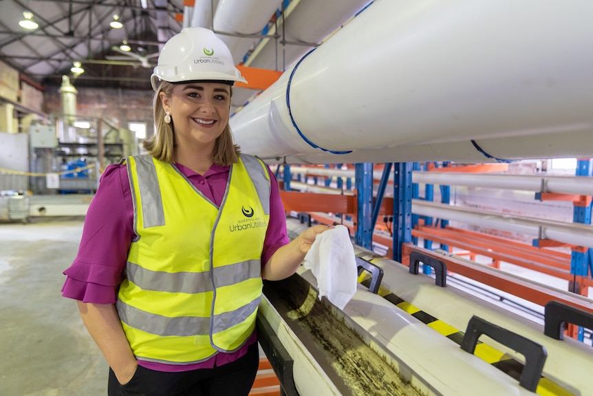A woman in high vis stands next to a pipe.