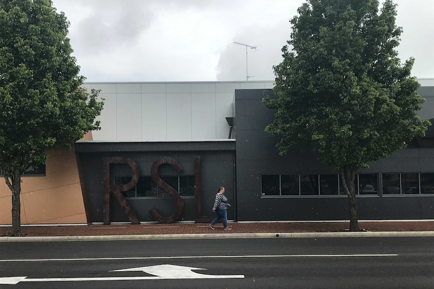 A woman walks in the rain in front of a grey building with huge RSL lettering