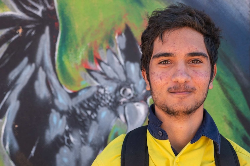 A young Indigenous man in a high visibility shirt smiles at the camera.