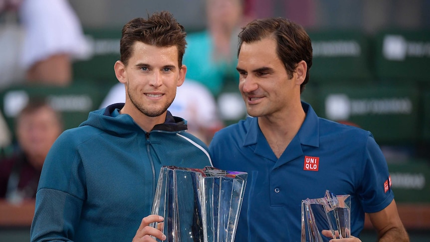 Dominic Thiem smiles while holding the Indian Wells trophy as Roger Federer looks at his opponent