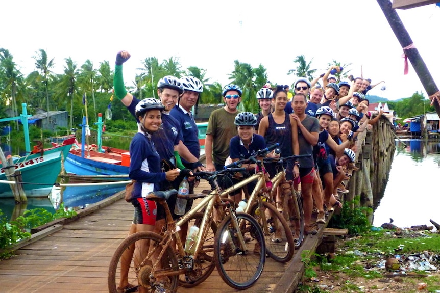 Group of cyclists in Cambodia surrounded by their bikes and coconut trees.