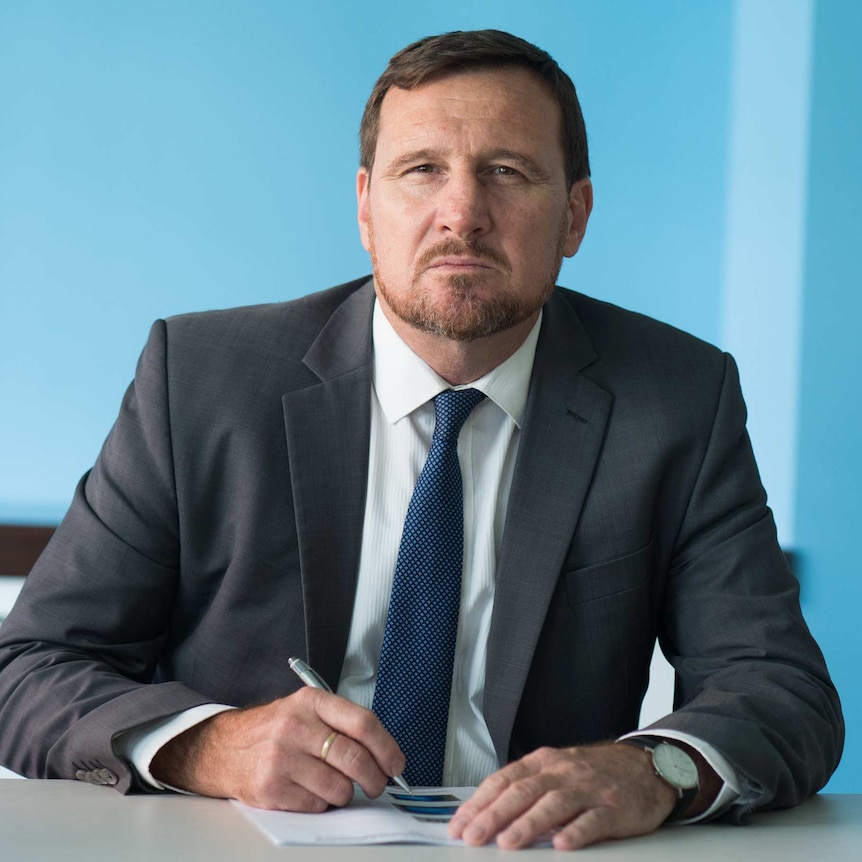 Gerard Dwyer, SDA national secretary, wearing a suit and sitting at a desk with a pen in hand.