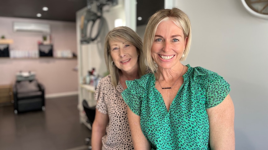 Two smiling women stand in a hairdressing salon.