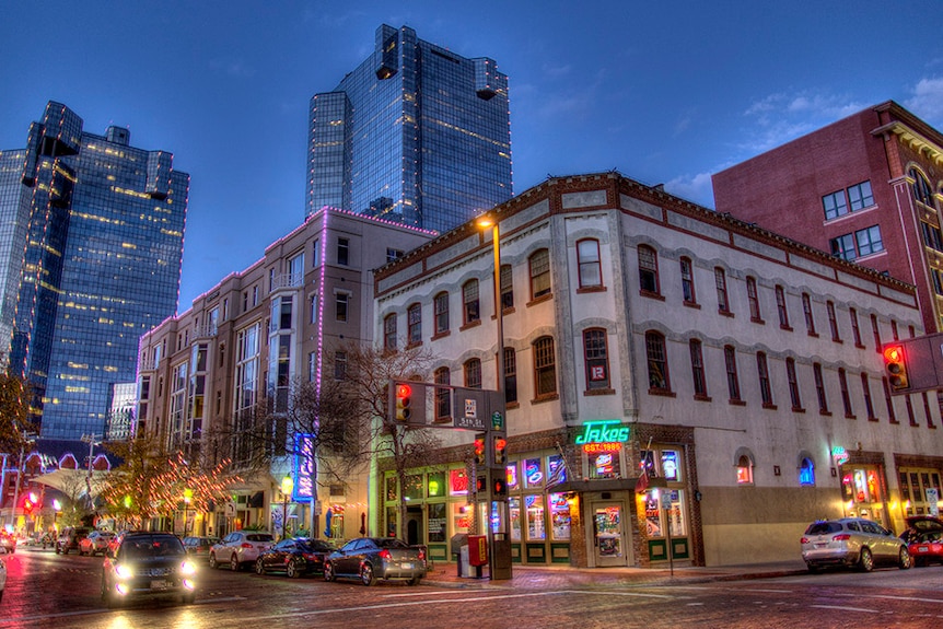 High-rise buildings and a row of restaurants light up the twilight sky over downtown Fort Worth.