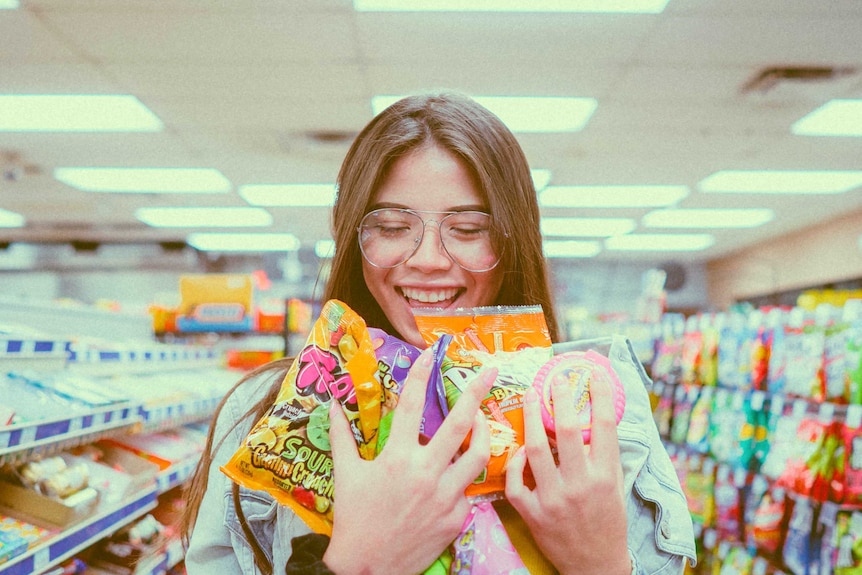 A woman holding lots of packets and smiling in a supermarket aisle for a story about whether loyalty programs are worth it.