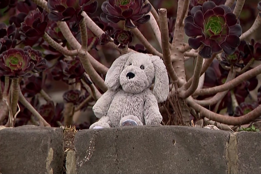 A plush toy sitting on a brick with trees in the background.