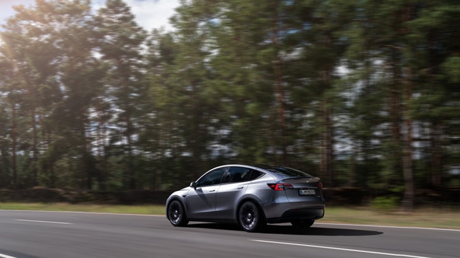 A sedan drives along a tree-filled road.